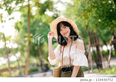 Portrait of asian young woman traveler with weaving hat and basket and a camera on green public park nature background. Journey trip lifestyle, world travel explorer or Asia summer tourism concept. Portrait of asian young woman traveler with weaving hat and basket and a camera on green public park nature background. Journey trip lifestyle, world travel explorer or Asia summer tourism concept. 110430752