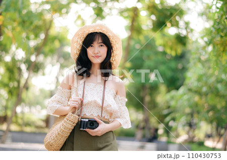 Portrait of asian young woman traveler with weaving hat and basket and a camera on green public park nature background. Journey trip lifestyle, world travel explorer or Asia summer tourism concept. 110430753