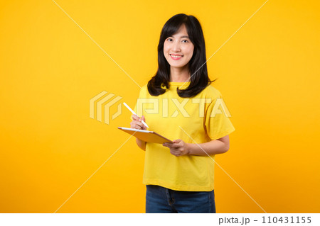 Experience the joy of education technology with portrait. A young Asian woman wearing a yellow t-shirt and denim jeans showcases a happy smile while using digital tablet. education technology concept. 110431155
