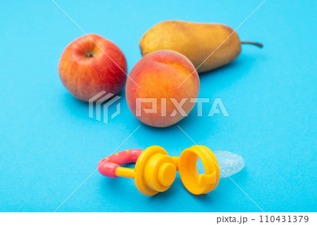 Apple, pear and peach with baby nibbler on a blue background. Concept of feeding fruits and vitamins to babies. Development of the chewing reflex in children, close-up Apple, pear and peach with baby nibbler on a blue background. Concept of feeding fruits and vitamins to babies. Development of the chewing reflex in children, close-up 110431379