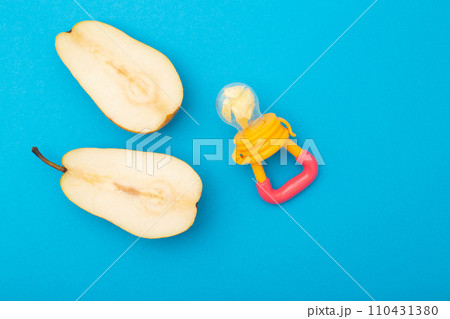 A pear cut in half on a blue background and a baby nibbler for feeding babies. Concept of the benefits of fruits and vitamins for babies. Copy space for text A pear cut in half on a blue background and a baby nibbler for feeding babies. Concept of the benefits of fruits and vitamins for babies. Copy space for text 110431380
