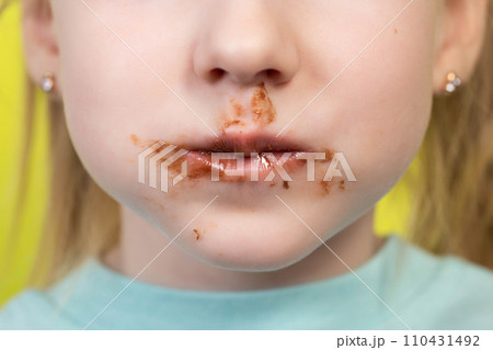 Little girl's mouth dirty with chocolate on a yellow background. Concept of children with a sweet tooth, close-up 110431492