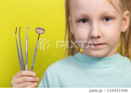 A beautiful seven-year-old girl holds dental instruments in her hand on a yellow background, close-up. The concept of therapeutic dentistry, root canal filling and teeth whitening. 110431496
