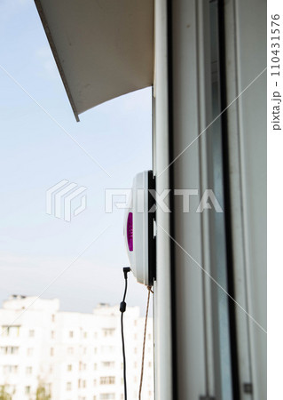 A modern vacuum robot window washer washes glass in an apartment on a balcony. View outside from the street. Safety from falls from a height. 110431576