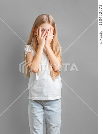 A little girl covering her face with her hands 110432673