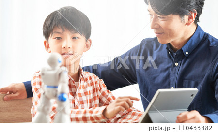 タブレットでロボットを動かす男の子とそれを見守る父親 110433882