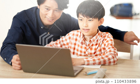 ノートパソコンの画面を見つめる男子小学生と大人の男性 110433896
