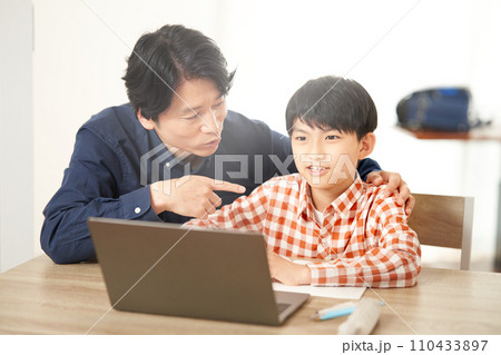 PCの前で勉強する小学生と話しかける父親 PCの前で勉強する小学生と話しかける父親 110433897
