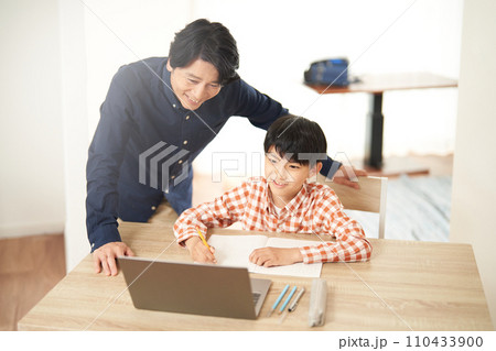 PCを見ながら勉強する男子小学生と笑顔で見守る父親 110433900