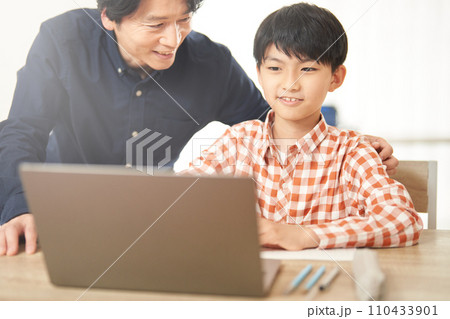PCを見ながら勉強する男子小学生とそれを見守る男性 110433901