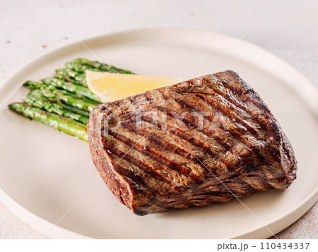 Grilled meat steak on plate with lemon and asparagus on white table background. Food and cuisine concept. Grilled meat steak on plate with lemon and asparagus on white table background. Food and cuisine concept. 110434337