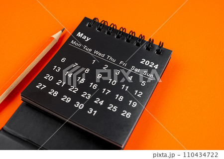 May 2024 desk calendar with pencil on orange background. 110434722