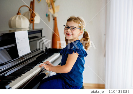 Beautiful little preschool girl playing piano at music school. Cute child having fun with learning to play music instrument. Early musical education for children 110435882