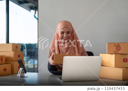 Muslim women selling online at home with box. Selling online with box to accept order from customer. Live stream selling online. muslim woman working smartphone and laptop at home 110437453