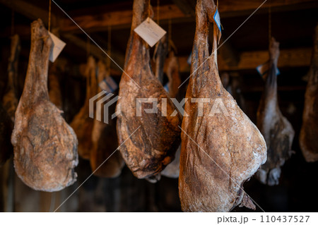 Aging hams hanging in traditional curing room Aging hams hanging in traditional curing room 110437527