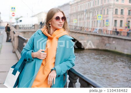 Woman walking through city near canal dressed in bright clothes orange hoodie Woman walking through city near canal dressed in bright clothes orange hoodie 110438482