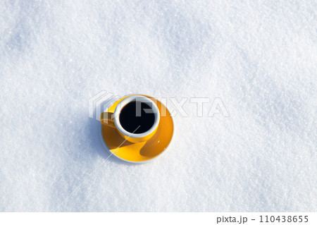 Winter background. Yellow cup with hot coffee or tea stands on the snow outdoor at sunny day with cold weather outdoors. Winter background. Yellow cup with hot coffee or tea stands on the snow outdoor at sunny day with cold weather outdoors. 110438655