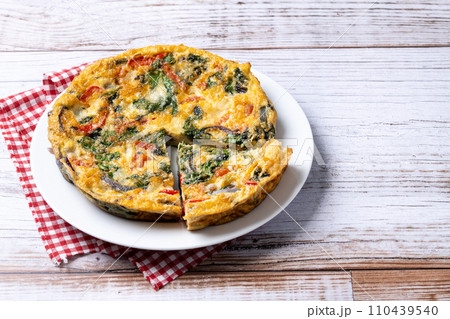 Italian Frittata made with spinach, tomatoes, onion and peppers on white wooden table 110439540