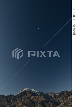 南アルプスの山並み、紺碧の空に浮かぶ月齢21.7下弦の月 110439860
