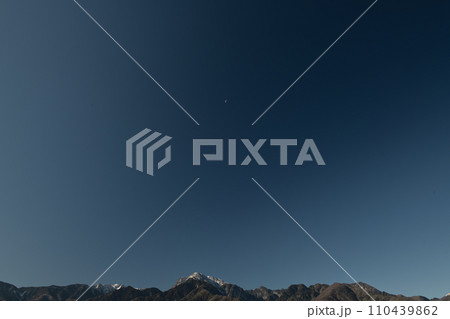 南アルプスの山並み、紺碧の空に浮かぶ月齢21.7下弦の月 110439862