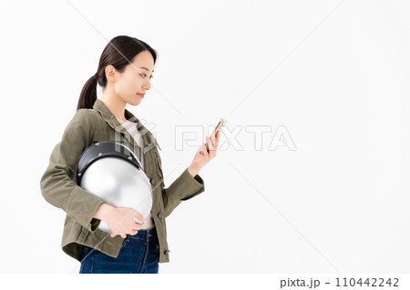 ヘルメットを抱えてスマートフォンを持つ女性 110442242