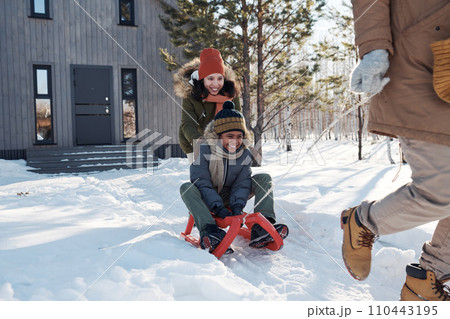 Happy young woman pushing son on sledge Happy young woman pushing son on sledge 110443195