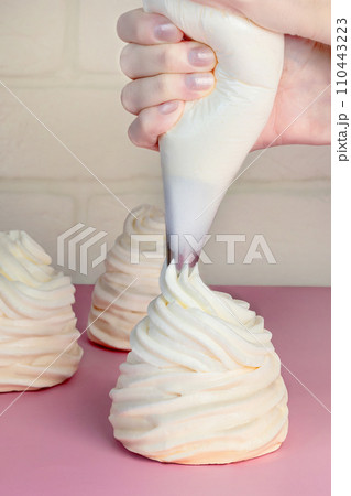 A woman makes Pavlova cakes, squeezes out the cream from a pastry envelope, vertical food photo A woman makes Pavlova cakes, squeezes out the cream from a pastry envelope, vertical food photo 110443223