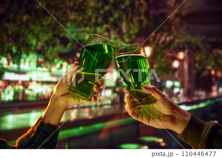 Two people sitting in pub at bar counter and drinking green traditional beer. Selective focus. Blurred. Two people sitting in pub at bar counter and drinking green traditional beer. Selective focus. Blurred. 110446477