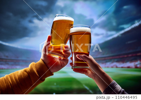 Two friends sitting at arena and drinking cold refreshing foamy beer and support their favorite football team during deciding match. 110446495