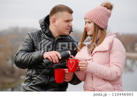 Young couple drinking a hot drink outside by the river 110446905