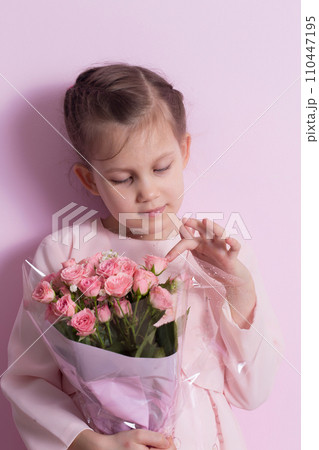 A cute little girl in a pink dress holds a bouquet of pink roses 110447195