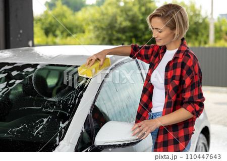 Blonde young woman washing car windscreen and looking involved 110447643