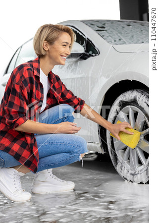 Blonde woman in checkered shirt washing a white car 110447670