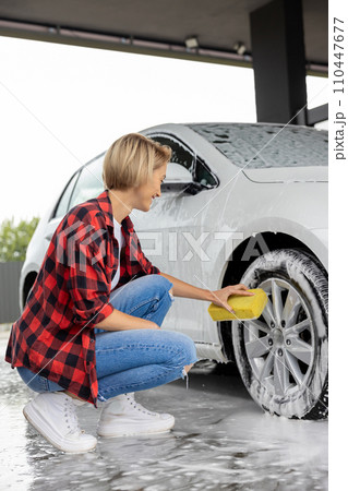 Blonde woman in checkered shirt washing a white car 110447677