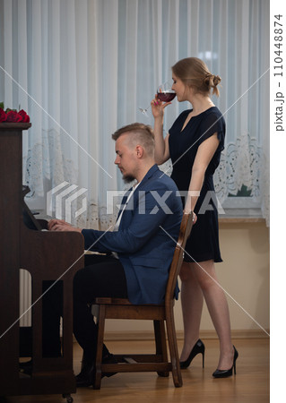 An elegantly dressed man plays a song on the piano. 110448874