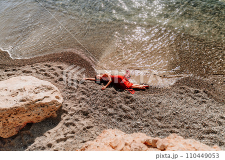 Woman red dress sea. Female dancer in a long red dress posing on a beach with rocks on sunny day 110449053