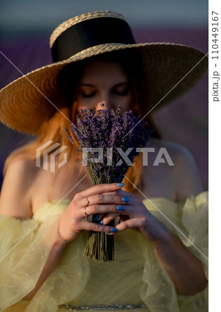 Lavender sunset girl. A laughing girl in a blue dress with flowing hair in a hat walks through a lilac field, holds a bouquet of lavender in her hands. 110449167