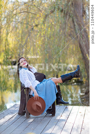 Autumn lake woman. She sits by a pond on a wooden pier in autumn and admires nature. The concept of tourism, weekends outside the city. 110449604