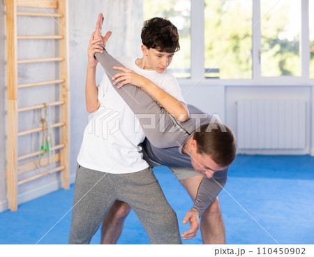 Teenage boy and middle-aged man training arm twist technique during self-defense courses 110450902