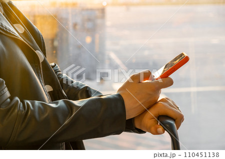Woman in a black jacket checking her smartphone standing with a suitcase at the airport. Woman in a black jacket checking her smartphone standing with a suitcase at the airport. 110451138