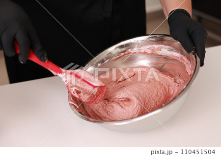 The pastry chef mixes silicone spatula the brown dough for the French desert macaron or macaroon in a stainless steel bowl, the process of preparing the cakes. Concept of confectionery or pastry shop The pastry chef mixes silicone spatula the brown dough for the French desert macaron or macaroon in a stainless steel bowl, the process of preparing the cakes. Concept of confectionery or pastry shop 110451504