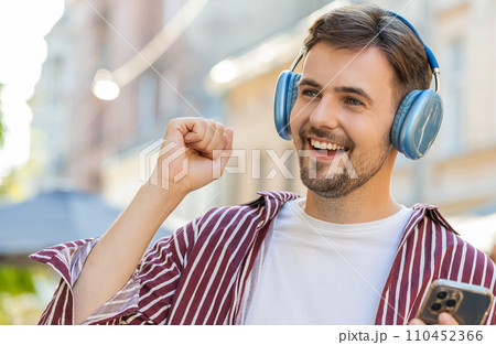 Happy bearded man in wireless headphones choosing, listening music dancing outdoors city street Happy bearded man in wireless headphones choosing, listening music dancing outdoors city street 110452366