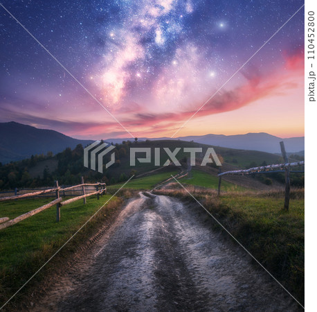 Milky Way over the rural road, wooden fence in mountains at night 110452800