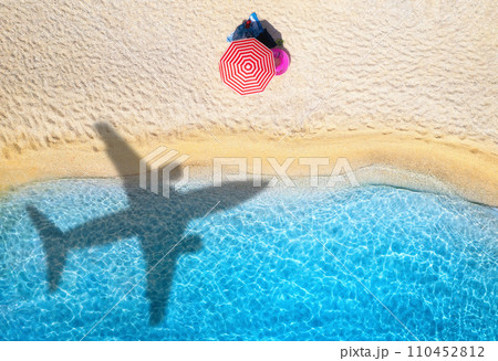 Aerial view of blue sea, airplane shadow, sandy beach, umbrella Aerial view of blue sea, airplane shadow, sandy beach, umbrella 110452812