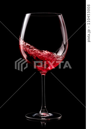 A glass with red wine is isolated on black background. Rose wine splashing in glassware. 110453008