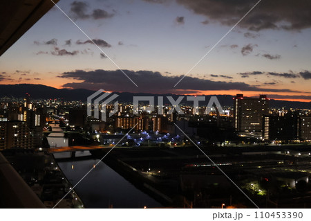 茜色に色づく空と青空と雲とまだ暗くネオンの見える都会の街並みの風景 茜色に色づく空と青空と雲とまだ暗くネオンの見える都会の街並みの風景 110453390