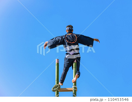 [東京・四谷] 高い竹梯子の頂上で空中に立ち、アクロバットを披露する後ろ姿の火消し。 110453546