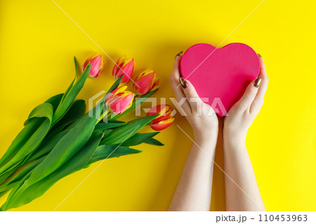 Female hands hold pink heart on yellow background. Tulips for valentine's day. 110453963