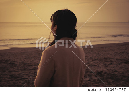 冬の海で夕焼けを楽しむ若い女性 冬の海で夕焼けを楽しむ若い女性 110454777