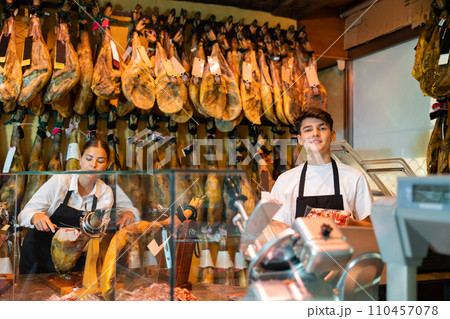 Girl and guy sellers of butcher shop working behind counter with Iberian jamon 110457078